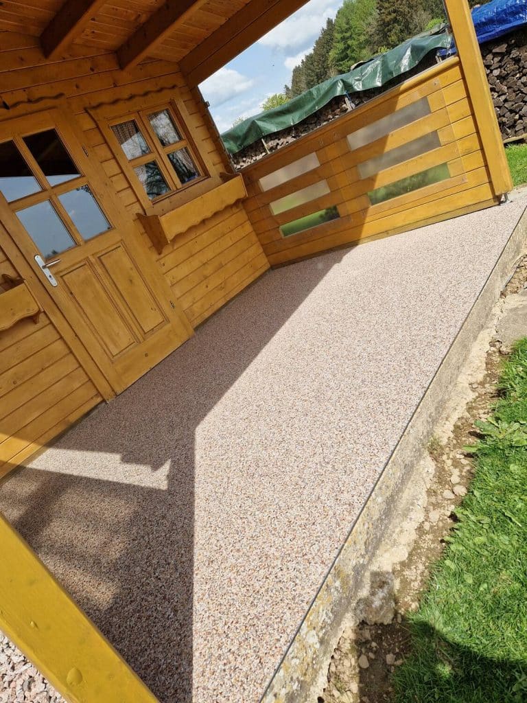 Terrasse en tapis de pierres beige devant un chalet en bois — pose Sol Color