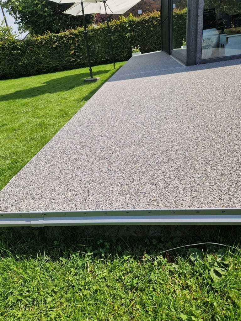 Terrasse en tapis de pierres gris clair le long d’une baie vitrée — réalisation Sol Color à Eupen